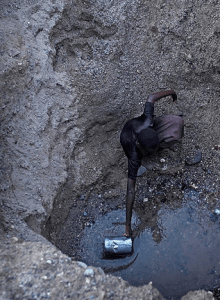 A Turkana woman scoops the remaining water from a well dug by hand.